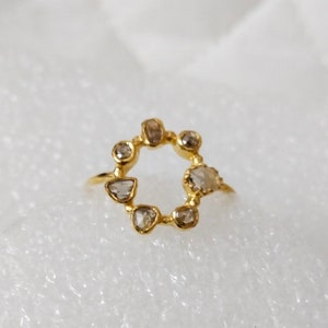May include: A gold ring featuring a circle of small, irregularly shaped diamonds. The diamonds are set in a gold band and arranged in a circle around the ring.