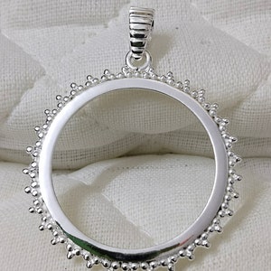 Peut inclure: Pendentif en argent avec un bord rond et perlé et une bélière simple. Le pendentif est conçu pour contenir une pièce de monnaie ou un autre objet rond.
