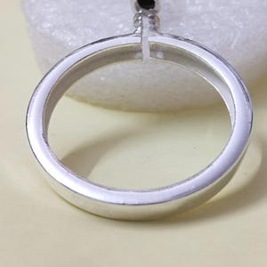 Könnte beinhalten: Nahaufnahme eines silberfarbenen Rings mit kreisförmigem Design. Der Ring hat ein kleines, dekoratives Oberteil. Der Ring besteht aus einem glänzenden Metallmaterial und ist vor einem hellen Hintergrund platziert.