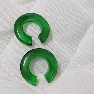 May include: Two green hoop earrings made of plastic. The earrings are thick and have a rounded shape.