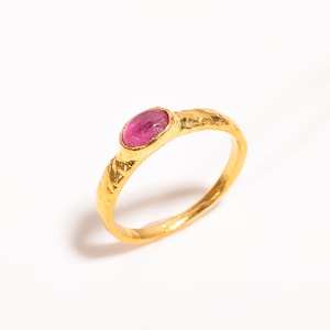 May include: A gold ring with a pink oval gemstone set in the centre. The band of the ring is textured and has a twisted design.