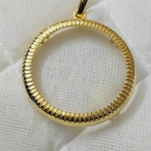 Puede incluir: Pendiente de moneda dorado con un borde texturizado y un bucle en la parte superior para colgar.