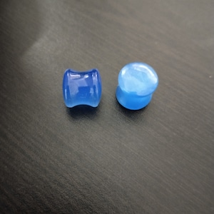 May include: Two blue ear gauges, one is a round shape and the other is a slightly curved cylinder shape.