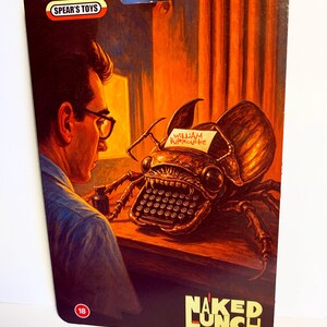 Puede incluir: Un paquete de juguetes vintage con ilustraciones de "Naked Lunch" de William Burroughs. La ilustraci&oacute;n muestra a un hombre con gafas mirando a una criatura-m&aacute;quina de escribir. El paquete tiene el logo "Spear's Toys" y una indicaci&oacute;n de edad "18".