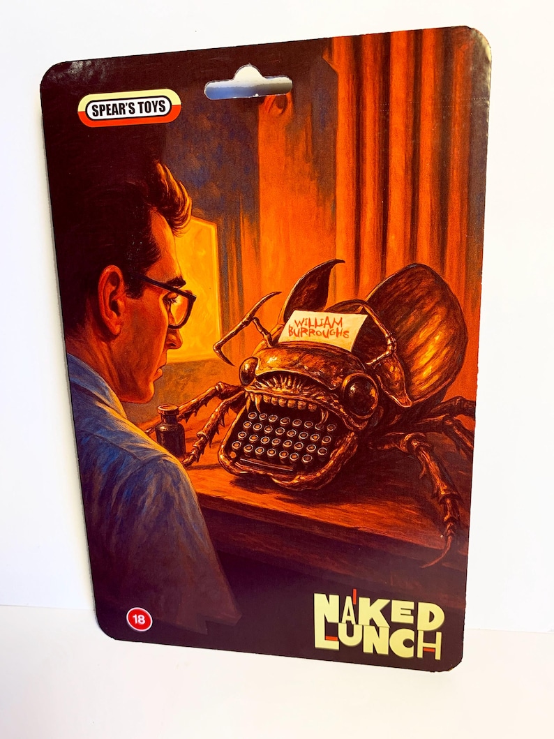 Puede incluir: Un paquete de juguetes vintage con ilustraciones de "Naked Lunch" de William Burroughs. La ilustraci&oacute;n muestra a un hombre con gafas mirando a una criatura-m&aacute;quina de escribir. El paquete tiene el logo "Spear's Toys" y una indicaci&oacute;n de edad "18".