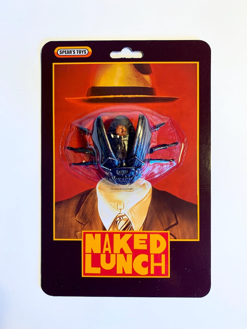 Puede incluir: Paquete de juguete con una cabeza de insecto negro con sombrero fedora y traje. El paquete tiene el texto "NAKED LUNCH" en amarillo y rojo. La marca "SPEAR'S TOYS" est&aacute; en la parte superior del paquete.