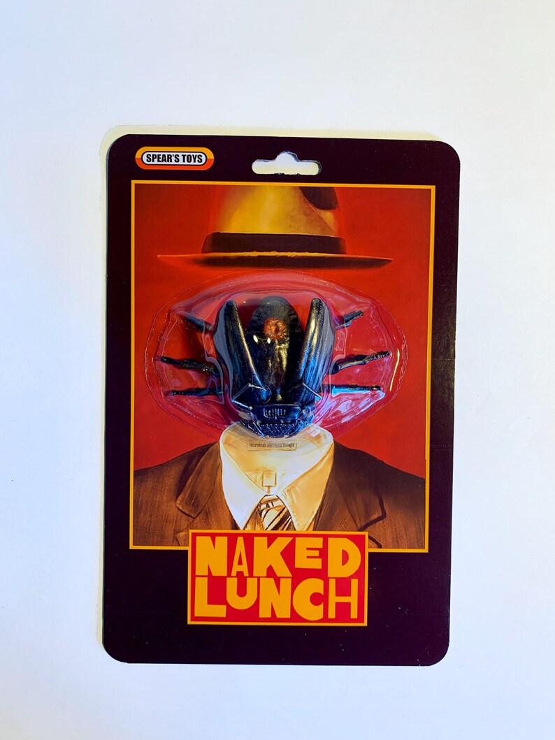 Puede incluir: Un paquete de figura de acci&oacute;n de estilo vintage con una cabeza de insecto negra y un sombrero fedora sobre un traje. El texto "NAKED LUNCH" est&aacute; en naranja. La marca "SPEAR'S TOYS" est&aacute; en la parte superior.