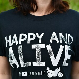 May include: Black t-shirt with white text that reads "HAPPY AND ALIVE" with a motorcycle graphic and the text "#  LAVI & OLLIE" below.
