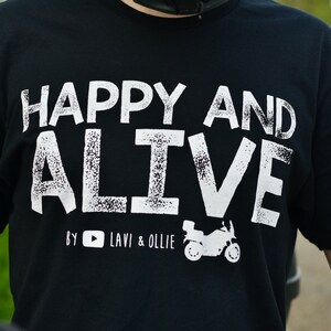 May include: Black t-shirt with white text that reads "Happy and Alive" with a small motorcycle graphic and the text "By YouTube Lavi & Ollie".