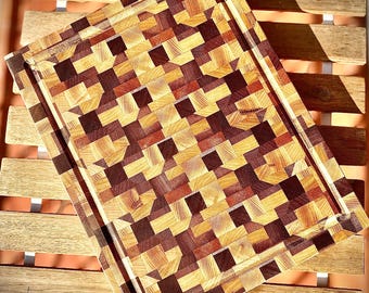 May include: A large wooden cutting board with a checkered pattern of different colored woods. The board has a raised edge around the perimeter.