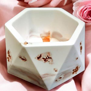May include: A white, geometric planter with copper-colored accents. The hexagonal-shaped container has a marbled effect with pink and gray tones. The planter is empty and sits on a pink surface, with pink roses in the background.