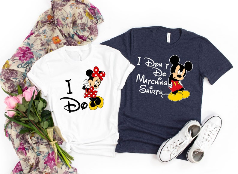 Op de afbeelding: Een wit T-shirt met de tekst "I Do" en een cartoon afbeelding van Minnie Mouse. Een donkerblauw T-shirt met de tekst "I Don't Do Matching Shirts" en een cartoon afbeelding van Mickey Mouse.