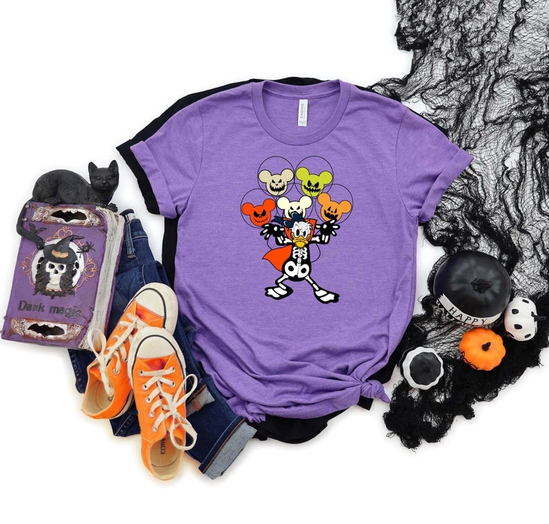 May include: Purple t-shirt with a skeleton Mickey Mouse holding up five Halloween-themed Mickey Mouse heads. The Mickey Mouse heads are orange, yellow, green, and red.