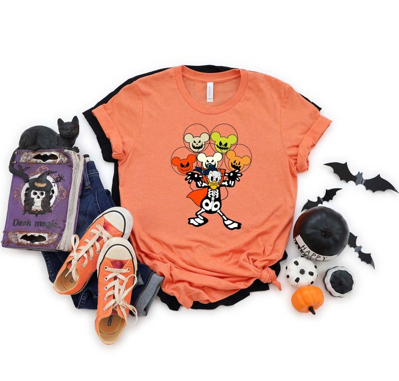 May include: Orange t-shirt with a black and white illustration of a skeleton Mickey Mouse holding a bunch of orange, yellow, and green balloons with Mickey Mouse faces. The balloons have spooky expressions.