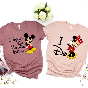 Op de afbeelding: Twee T-shirts met een Disney-thema. Het roze shirt zegt "Ik doe het" met een afbeelding van Minnie Mouse. Het mauve shirt zegt "Ik doe geen matchende shirts" met een afbeelding van Mickey Mouse.