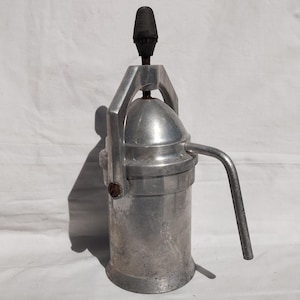 May include: A silver aluminum stovetop espresso maker with a black plastic handle and a spout. The maker has a round body and a cylindrical base.