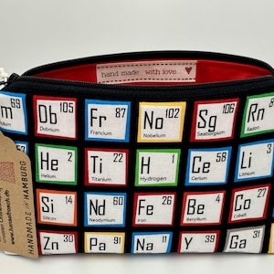 Könnte beinhalten: Eine Kosmetiktasche mit Reißverschluss und schwarzem Hintergrund mit einem Periodensystem-Design. Die Tasche hat ein rotes Innenfutter und ein Etikett mit der Aufschrift "handgemacht mit Liebe". Die Tasche ist ca. 25 cm breit.