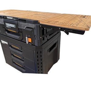 May include: A black and gray TOUGHBUILT StackTech rolling workbench with a wooden fold-out work surface. The workbench has drawers and storage compartments. The work surface has measurement markings.