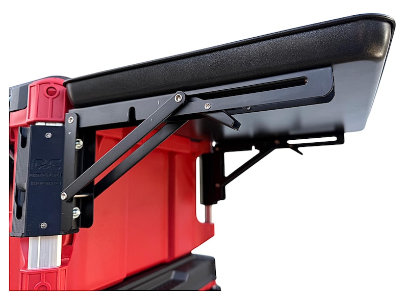 May include: A black folding table with a black top and a red base. The table is attached to a red cooler with a black hinge. The table is in the up position.
