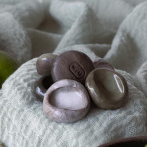 May include: A small bowl filled with lime wedges sits on a green cloth with a pile of small gray and brown stones. The stones have a small indentation in the center.