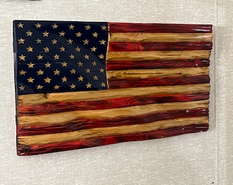 May include: A wooden American flag with red, white, and blue stripes. The stars are gold and the stripes are made of different types of wood.