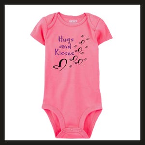 Pode incluir: Um body rosa para beb&eacute; com mangas curtas. O body apresenta o texto "Hugs and Kisses" em roxo e gr&aacute;ficos de cora&ccedil;&otilde;es pretos. A marca "Carter's" &eacute; vis&iacute;vel no topo. A pe&ccedil;a de roupa tem fechos de press&atilde;o na parte inferior.