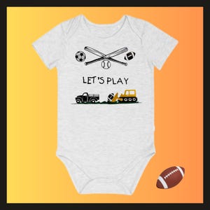 May include: A light gray baby onesie with a graphic of sports equipment and vehicles. The design includes crossed baseball bats, a soccer ball, a baseball, and a football. The text "LET'S PLAY" is printed above a truck and a construction vehicle.