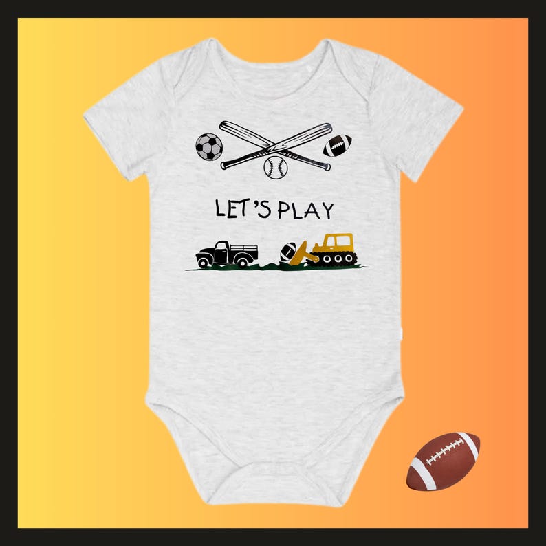 May include: A light gray baby onesie with a graphic of sports equipment and vehicles. The design includes crossed baseball bats, a soccer ball, a baseball, and a football. The text "LET'S PLAY" is printed above a truck and a construction vehicle.
