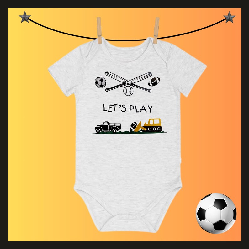 May include: A white baby onesie with a graphic design featuring a soccer ball, baseball bat, baseball, football, and the text "LET'S PLAY." Below are illustrations of a truck and a construction vehicle.