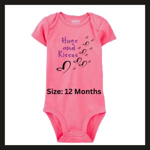 Pode incluir: Um body rosa para beb&eacute; com mangas curtas. O body tem as palavras "Hugs and Kisses" em roxo e preto, com gr&aacute;ficos de cora&ccedil;&otilde;es. O tamanho &eacute; 12 meses.