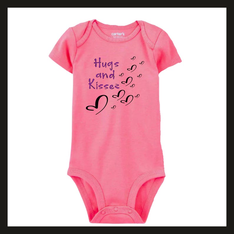 Pode incluir: Um body rosa para beb&eacute; com mangas curtas. O body apresenta o texto "Hugs and Kisses" em roxo e gr&aacute;ficos de cora&ccedil;&otilde;es pretos. A marca "Carter's" &eacute; vis&iacute;vel no topo. A pe&ccedil;a de roupa tem fechos de press&atilde;o na parte inferior.