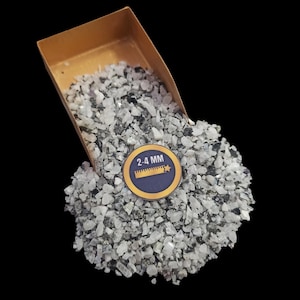 May include: A close-up of a small scoop filled with white and gray gravel. The gravel is labeled "2-4 MM" and is likely used for landscaping or decorative purposes.