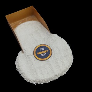 May include: A white fine sand in a gold scoop with a blue and gold label that says "FINE SAND" with a ruler icon and a star.