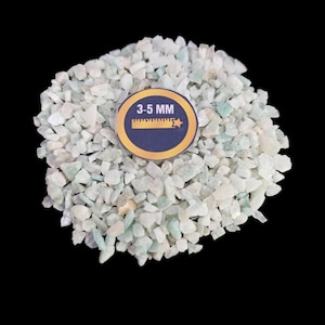 Op de afbeelding: Een close-up van een stapel kleine, lichtgroene en witte getrommelde stenen. De stenen zijn ongeveer 3-5 mm groot. Een liniaal met de tekst "3-5 MM" is zichtbaar in de afbeelding.