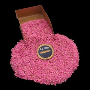 Może przedstawiać: Mała, brązowa metalowa łopatka wypełniona drobnym różowym piaskiem. Etykieta na piasku głosi "0,5-1MM".