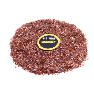 May include: A pile of small, pink, iridescent glass chips, approximately 0.5-1 mm in size. The glass chips are arranged in a circle on a white background. A small, yellow label with the text "0.5-1MM" is placed on top of the glass chips.