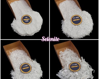 May include: Four containers of selenite crystals in various sizes. The containers are made of brown cardboard and are filled with white selenite crystals. The crystals are labeled with their size in millimeters: Fine Sand, 0.5-1mm, 1-3mm, and 3-5mm.