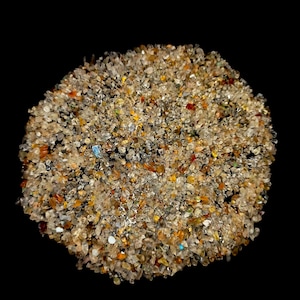 Puede incluir: Primer plano de un montón grande de pequeños cristales de cuarzo claros y translúcidos. Los cristales son de varios tonos de marrón, amarillo y naranja, con algunos cristales azules y verdes mezclados.