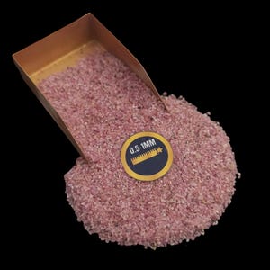 May include: A copper scoop filled with pink sand, with a label that reads "0.5-1MM" and a ruler icon. The sand is spilling out of the scoop onto a black background.