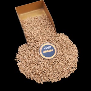 Puede incluir: Primer plano de un montón de pequeñas piedras de color marrón claro, de forma irregular. Las piedras están en una pala de metal dorado y se están derramando sobre un fondo negro. Una etiqueta negra y dorada con el texto "1-3 MM" es visible en el centro de la imagen.