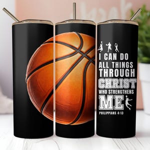Op de afbeelding: Zwarte beker met een basketbalontwerp. De oranje en bruine basketbalafbeelding staat op een zwarte achtergrond. De beker heeft ook de tekst "Ik kan alle dingen doen door Christus die mij sterkt" en basketbalsilhouetten.