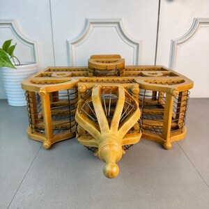 May include: A wooden birdcage with a decorative, ornate design. The cage is made of light brown wood and has a wire mesh interior. The cage has a pointed top and a decorative finial.
