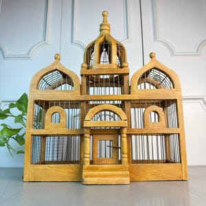 May include: A large, wooden birdcage with a domed top and intricate details. The cage is made of natural wood and has a wire mesh interior. The cage has a small door on the front and is decorated with decorative accents.
