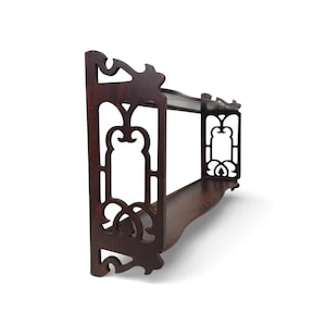 May include: Dark brown wooden wall shelf with ornate cut-out designs. The shelf has two tiers and decorative edges. The wood has a rich, warm tone, and the design is symmetrical and detailed. The shelf is designed to be mounted on a wall.