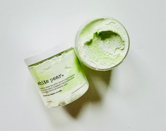 May include: Two jars of white pear scented sugar scrub. The jars are white with black text that reads "white pear.  infused sweet tea with sparkling bergamot with kissed pear - Pungent lemon enhanced with peach and wood bottom note.  Foaming sugar scrub".