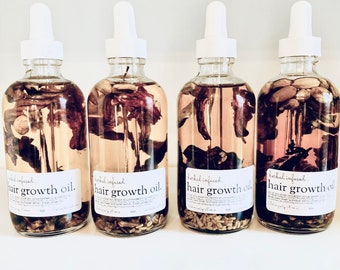 May include: Four clear glass bottles with dropper tops filled with a light brown liquid and dried herbs. Each bottle has a white label with the text "herbal infused hair growth oil."