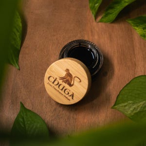 May include: A small, round, wooden container with a black lid. The container has a brown monkey logo and the text "CHUGA" with the words "Pure Himalayan Shilajit" underneath.