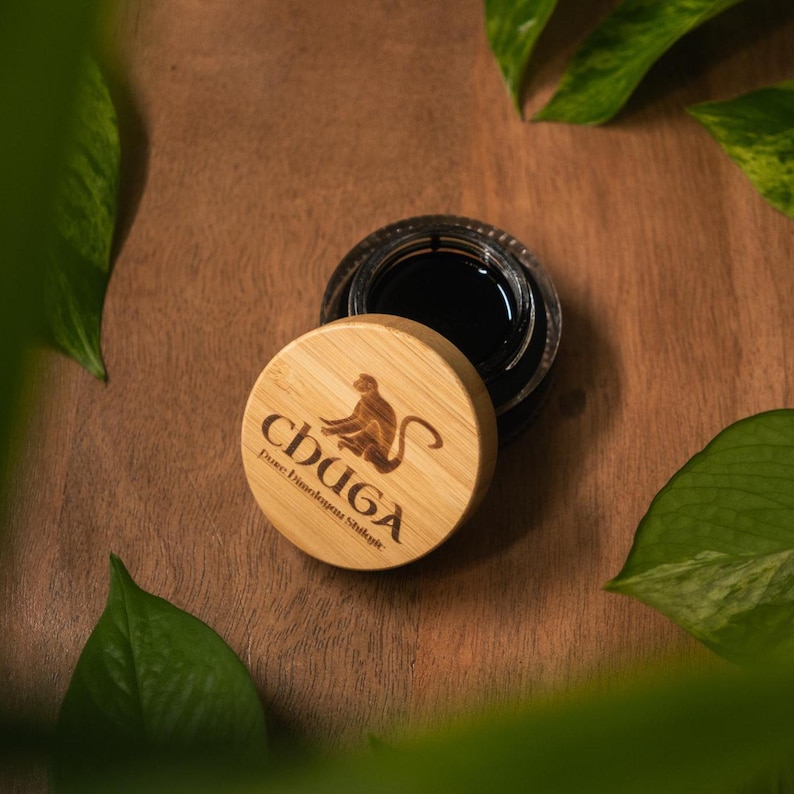 May include: A small, round, wooden container with a black lid. The container has a brown monkey logo and the text "CHUGA" with the words "Pure Himalayan Shilajit" underneath.