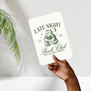 Op de afbeelding: Witte kaart met groene tekst die "Late Night Book Club est. 2024 just one more chapter" luidt. Een groene illustratie van een kat die een boek leest met een kopje koffie ernaast.