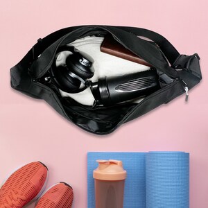 Puede incluir: Una bolsa de deporte negra con cierre de cremallera, que contiene una botella de agua, auriculares y una toalla. La bolsa est&aacute; abierta y el contenido es visible.